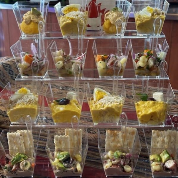 A tiered display of Peruvian appetizers in clear square cups, including ceviche and causa.