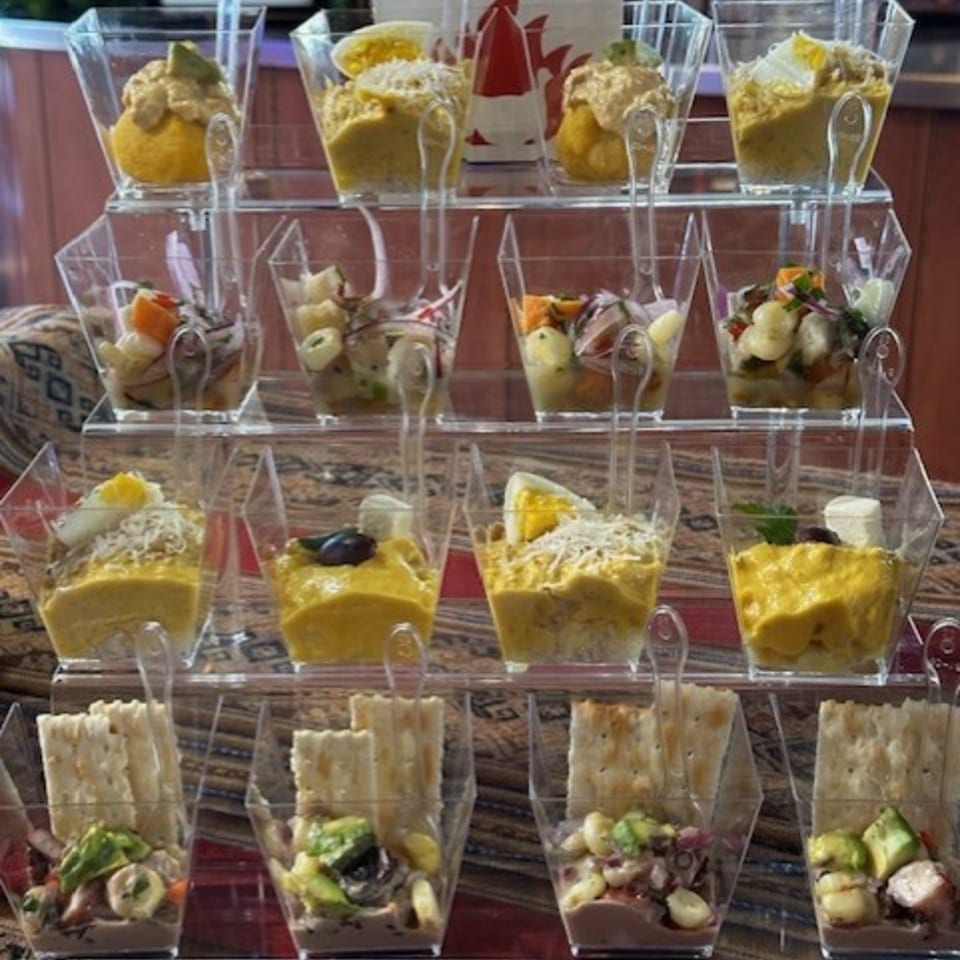 A tiered display of Peruvian appetizers in clear square cups, including ceviche and causa.