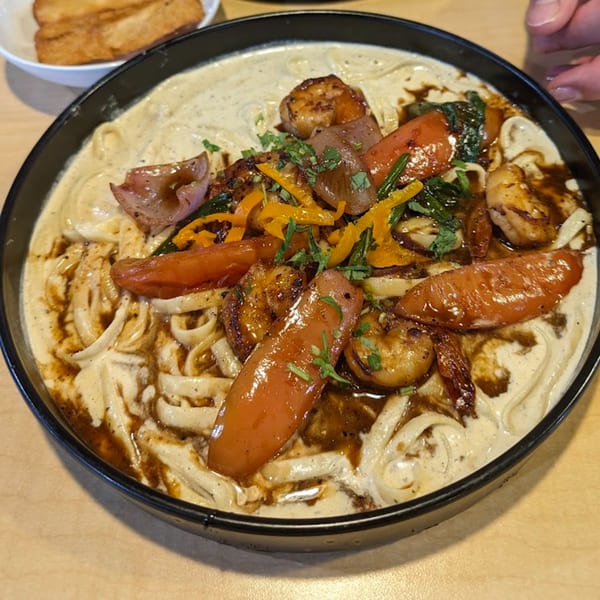 Peruvian Lomo Saltado with shrimp, vegetables, and noodles in a creamy sauce, served in a black bowl.
