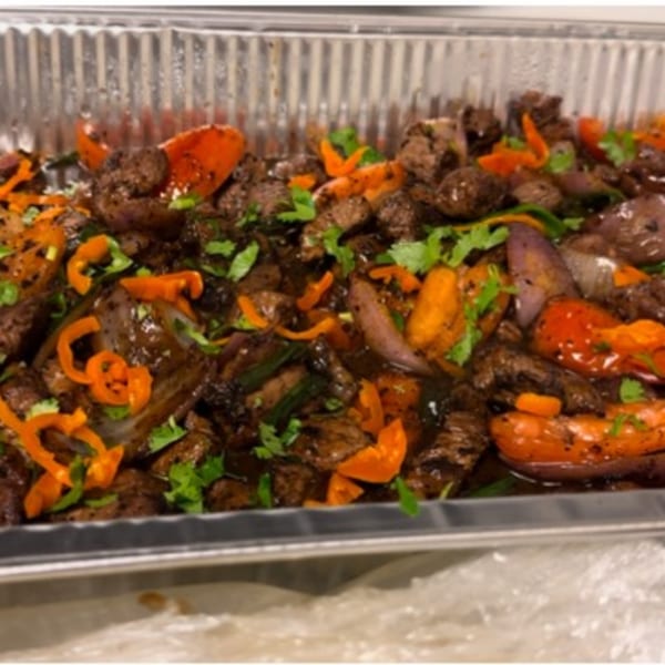 Peruvian Lomo Saltado with beef, red onions, tomatoes, and cilantro in a catering tray.