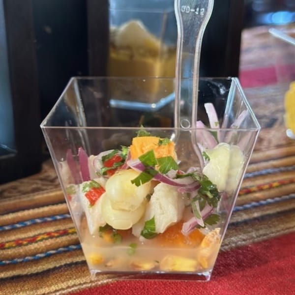 Peruvian ceviche in a clear square cup with a plastic spoon, on a colorful striped tablecloth.