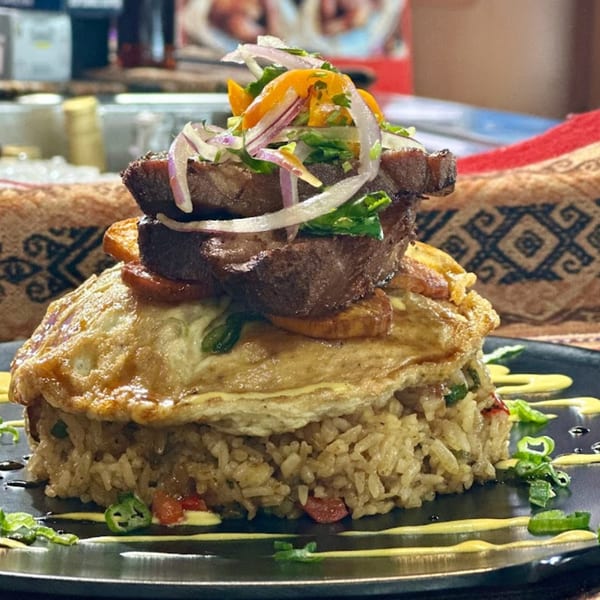 Peruvian Lomo Saltado with steak, fried egg, rice, and vegetables on a black plate.