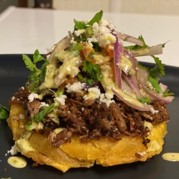 Peruvian dish with shredded meat, red onions, cilantro, and cheese on a fried plantain.