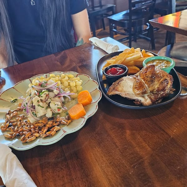 Peruvian ceviche with corn and sweet potato, alongside roasted chicken with fries and sauces on a wooden table.