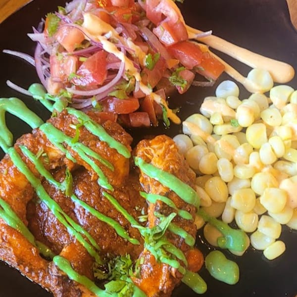 Peruvian chicken with green sauce, a side of corn, and a tomato and onion salad.