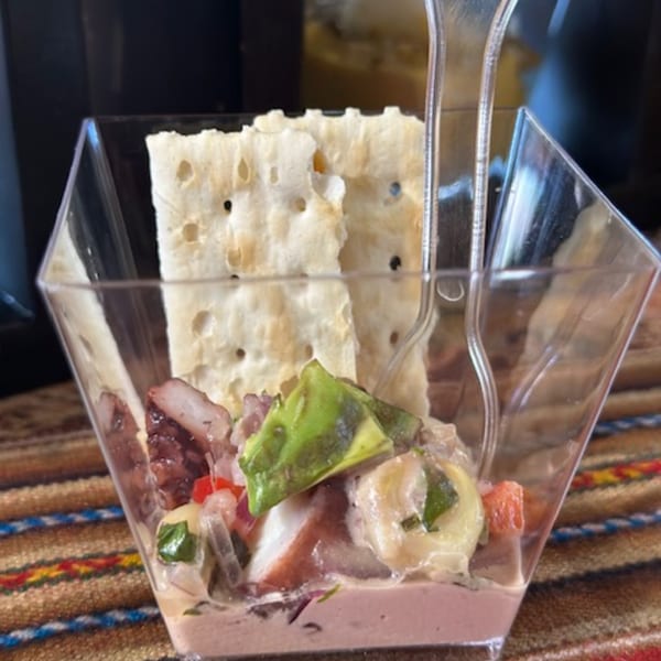 Peruvian ceviche with octopus, avocado, and crackers in a clear square glass.