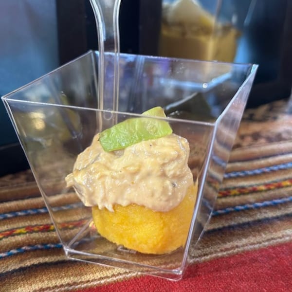 Peruvian causa appetizer with yellow potato, creamy topping, and a green garnish in a clear cup.