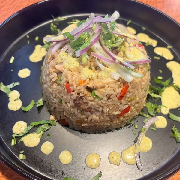 Peruvian chaufa rice with red onions, cilantro, and yellow sauce on a black plate.