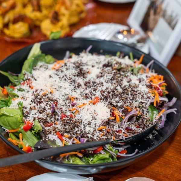 A large black bowl of fresh salad with greens, shredded carrots, red onions, and a topping of quinoa and cheese.