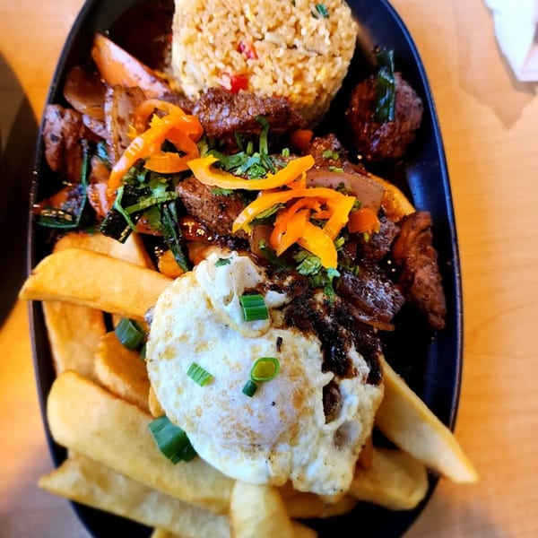 Peruvian Lomo Saltado with steak, fries, fried egg, rice, bell peppers, and cilantro on a black plate.