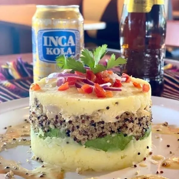 Peruvian causa with quinoa and avocado, topped with tomatoes and onions, next to an Inca Kola can.